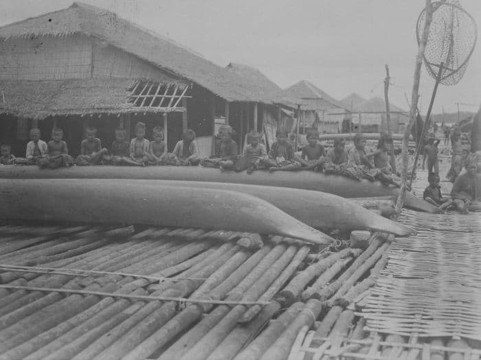 foto. Een rij kinderen op de rug van een prauw in een paaldorp in de Segara Anakan (Kinderzee)